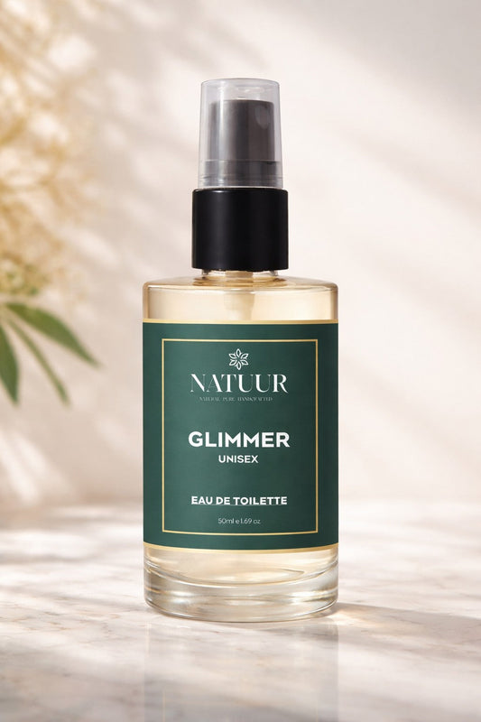 Natuur.in Glimmer unisex eau de toilette in a glass spray bottle with a dark green label on a sunlit marble surface.